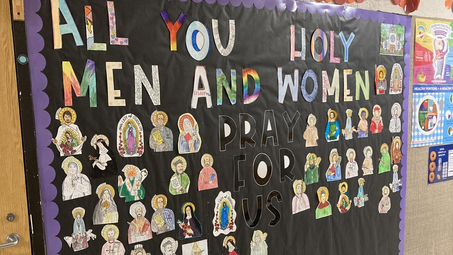 Image of a bulletin board with wording that says "All You Holy Men and Women" with images of saints below it.