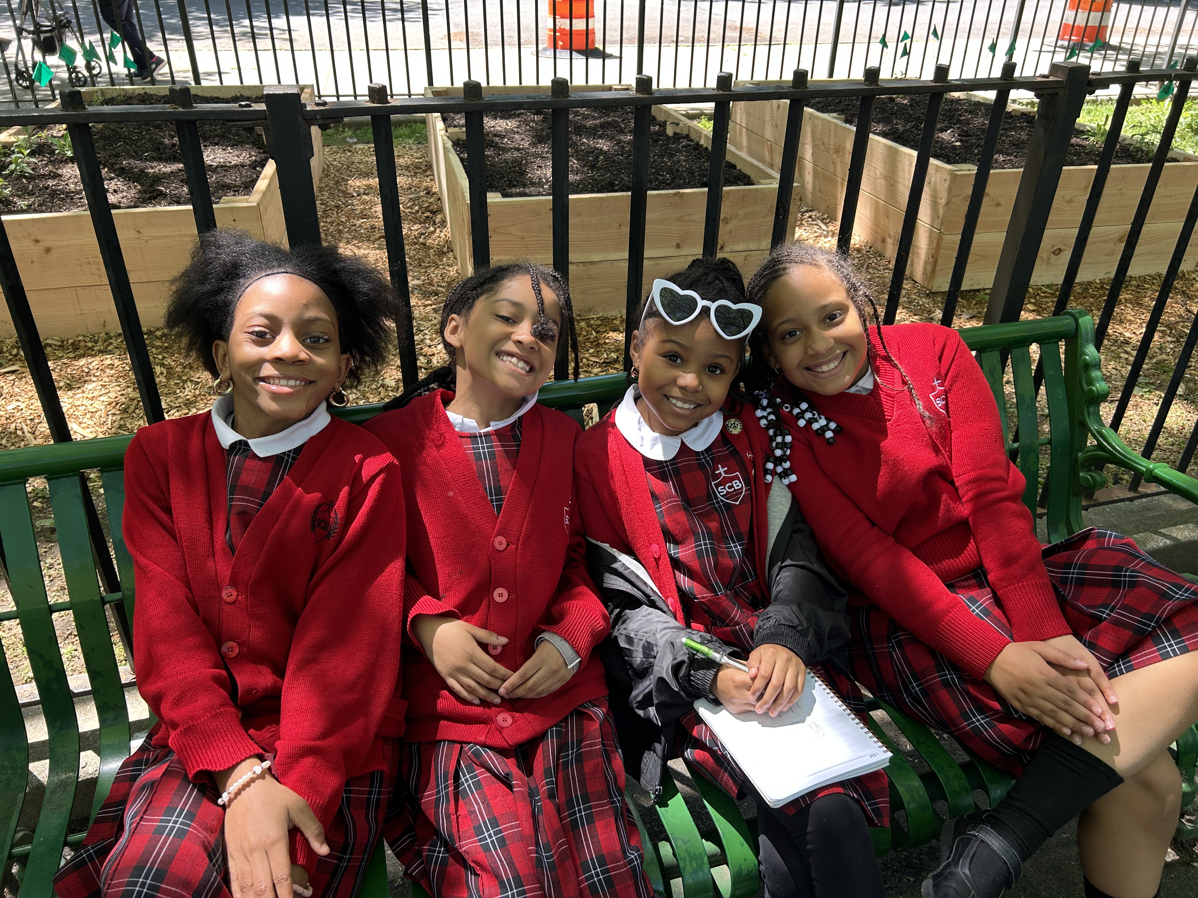 Image of four students in red school uniforms sitting on a green bench outside