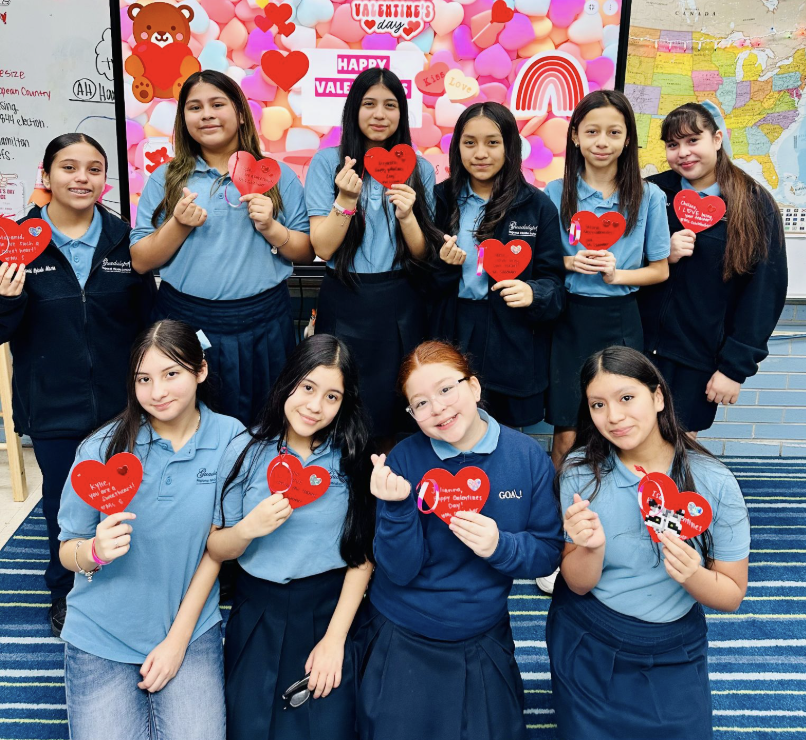 Image of students in two rows posing with red heart cutouts